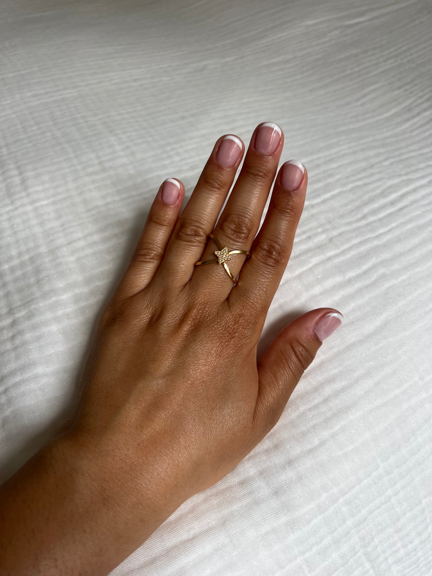Bague en acier inoxydable doré ornée d'un pendentif étoile incrusté de strass, portée sur une main avec une manucure française. Bijou élégant et raffiné de la collection Bisou Bijoux Paris.