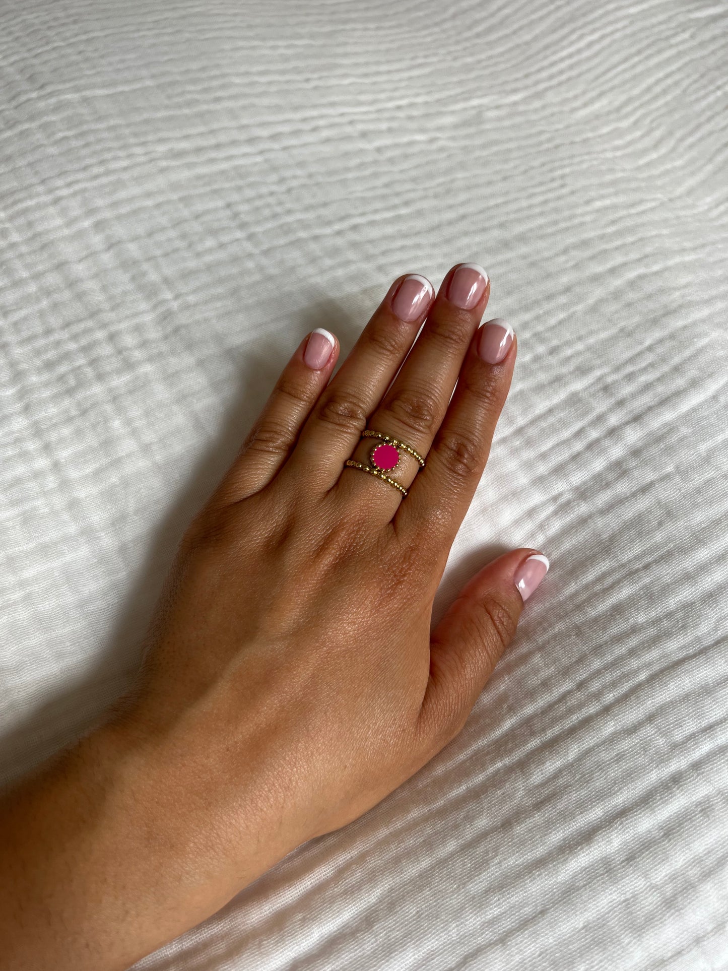 Bague en acier inoxydable doré ornée d'une pierre rose, portée sur une main avec une manucure française. Bijou élégant et coloré de la collection Bisou Bijoux Paris.