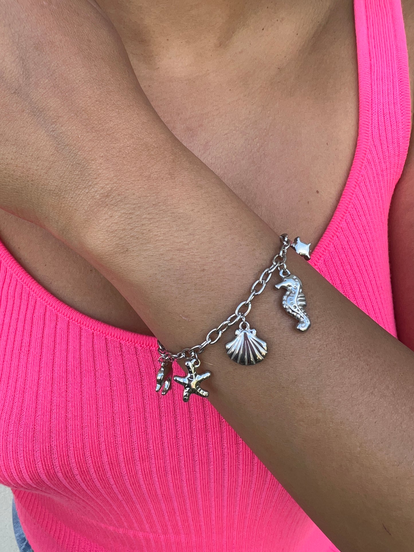Bracelet en acier inoxydable argenté orné de charms marins : étoile de mer, coquillage, hippocampe et étoile, porté sur un poignet féminin. Bijou estival et élégant de la collection Bisou Bijoux Paris.