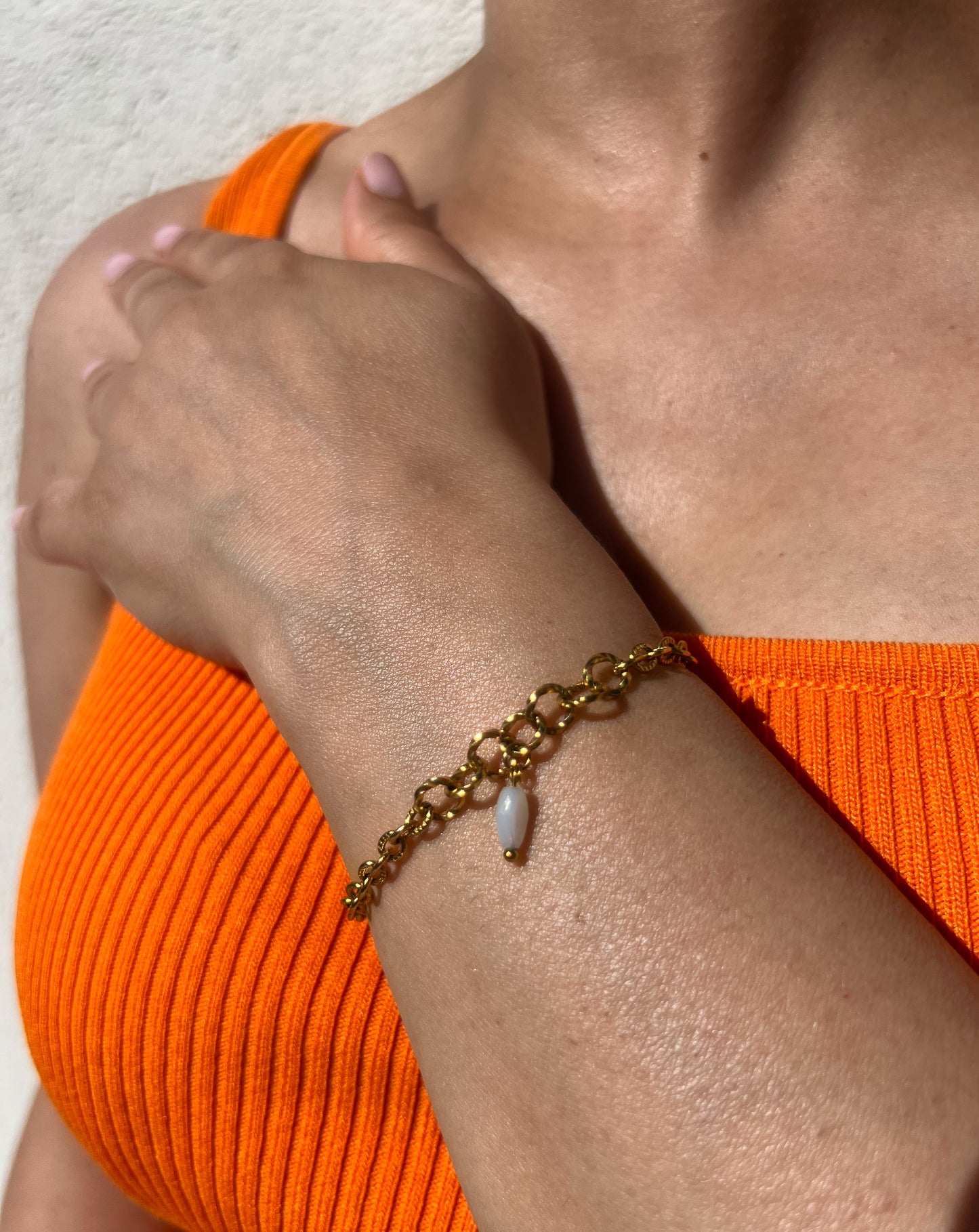 Bracelet en acier inoxydable doré avec grands maillons et pendentif goutte blanche, porté sur un poignet féminin. Bijou élégant et original de la collection Bisou Bijoux Paris.