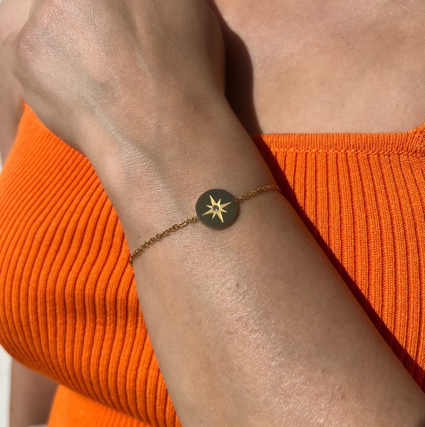 Bracelet en acier inoxydable doré avec médaille gravée d'une étoile du Nord et incrustée d'un cristal, porté sur un poignet féminin. Bijou symbolique et raffiné de la collection Bisou Bijoux Paris.
