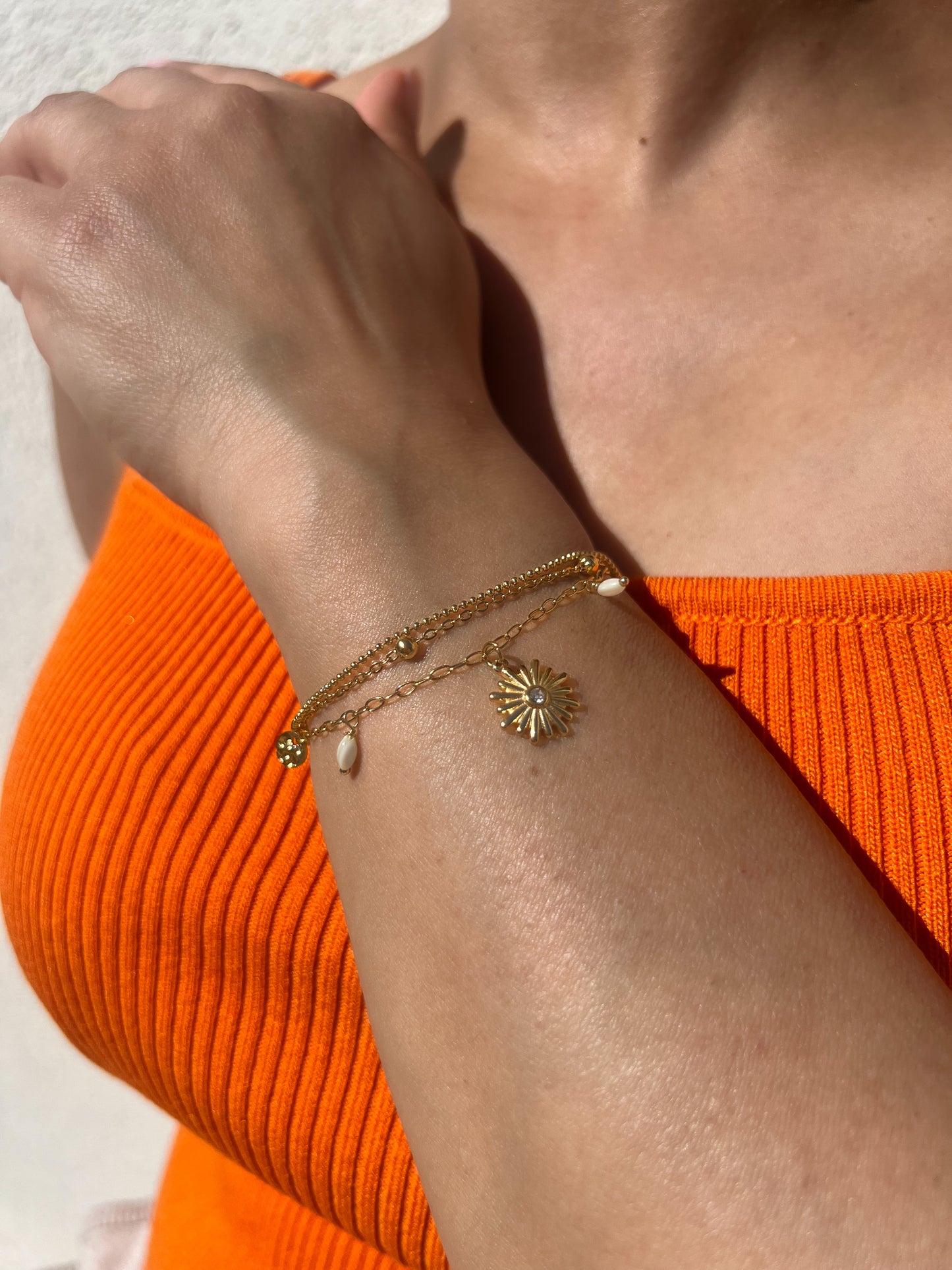 Bracelet en acier inoxydable doré avec pendentif fleur et perles, porté sur un poignet féminin. Bijou élégant et tendance de la collection Bisou Bijoux Paris.