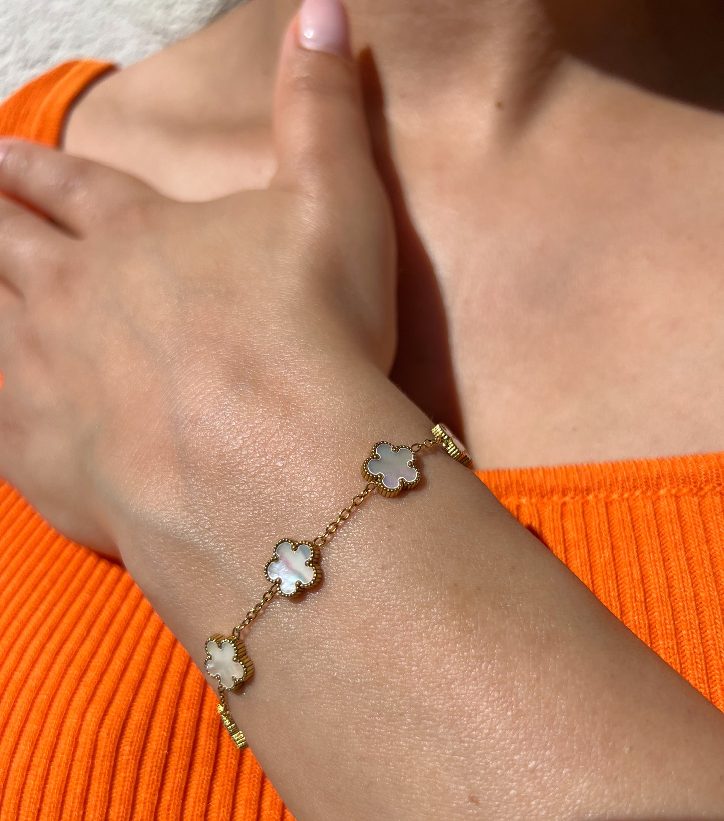 Bracelet en acier inoxydable doré orné de pendentifs trèfles en nacre, porté sur un poignet féminin. Bijou raffiné et intemporel de la collection Bisou Bijoux Paris.
