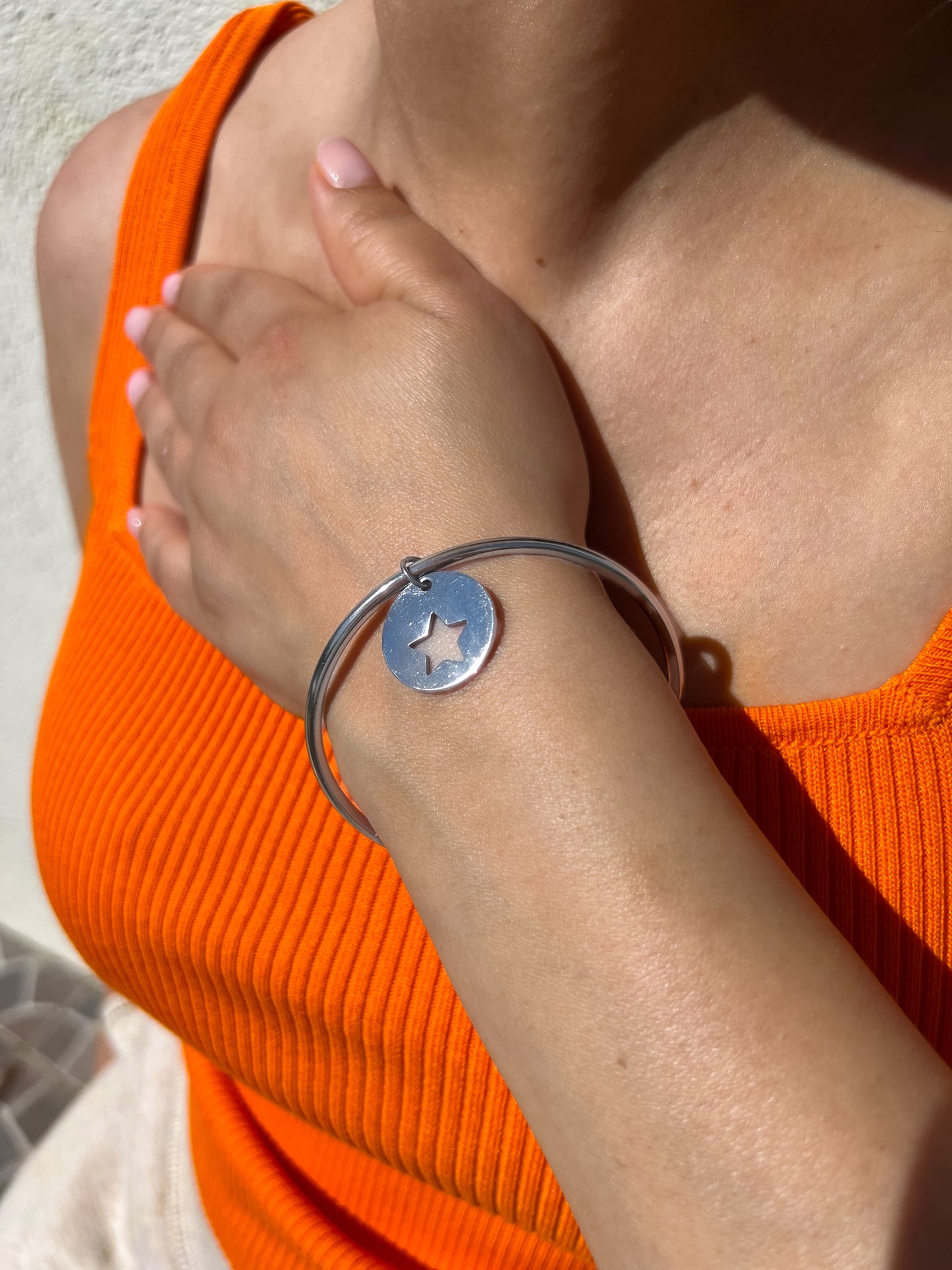 Bracelet jonc en acier inoxydable argenté avec une médaille étoile découpée, porté sur un poignet féminin. Bijou minimaliste et élégant de la collection Bisou Bijoux Paris.