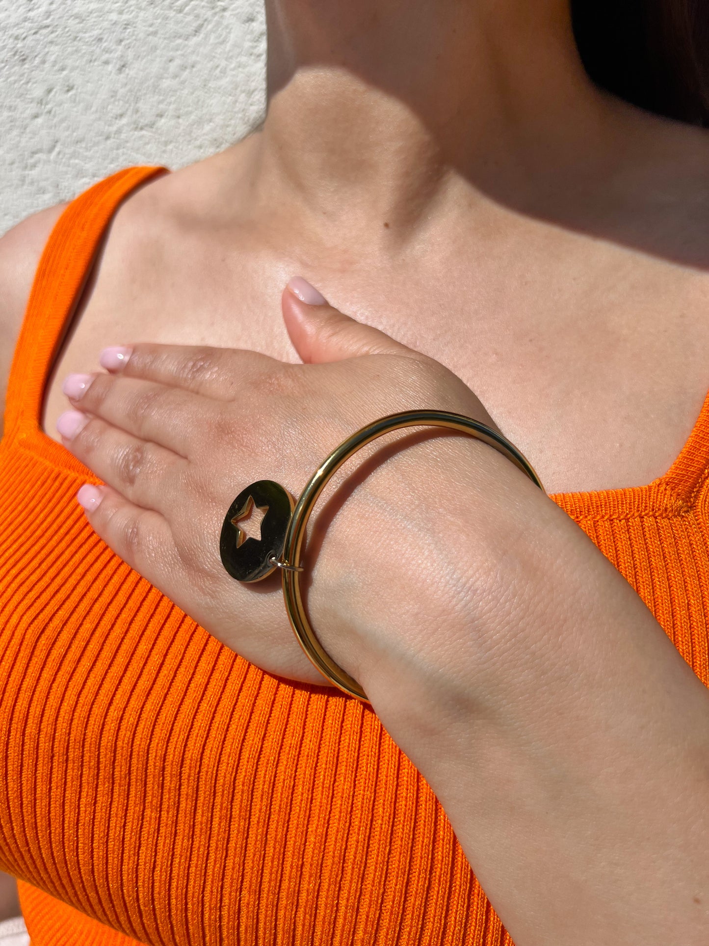 Bracelet jonc en acier inoxydable doré avec une médaille étoile découpée, porté sur un poignet féminin. Bijou minimaliste et moderne de la collection Bisou Bijoux Paris.
