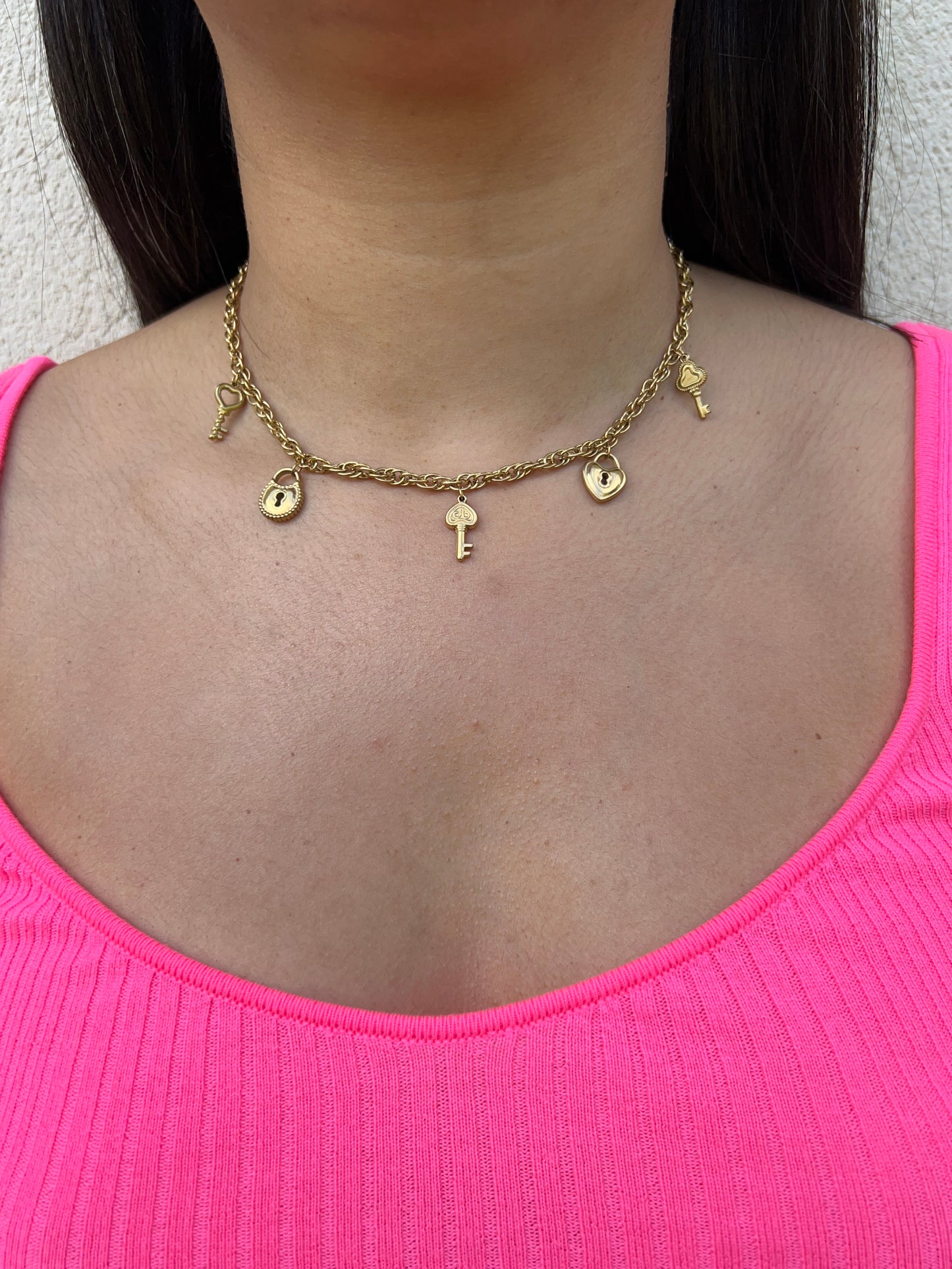 Collier en acier inoxydable doré avec une maille gourmette, orné de pampilles représentant des clefs, des cadenas et des coeurs, porté autour du cou féminin. Bijou symbolique et tendance de la collection Bisou Bijoux Paris.