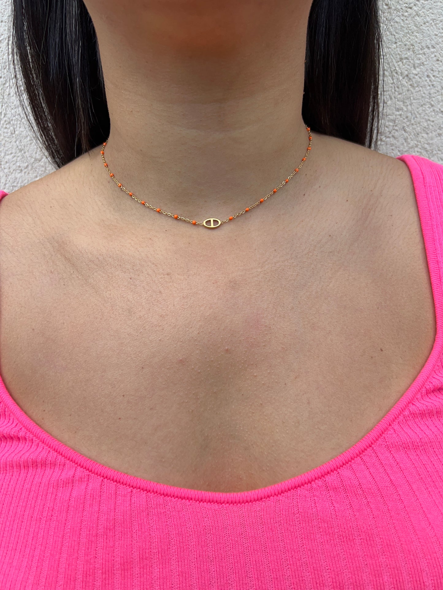 Collier en acier inoxydable doré, orné de perles orange et d'un pendentif ovale délicat, porté autour du cou féminin. Bijou coloré et raffiné de la collection Bisou Bijoux Paris.