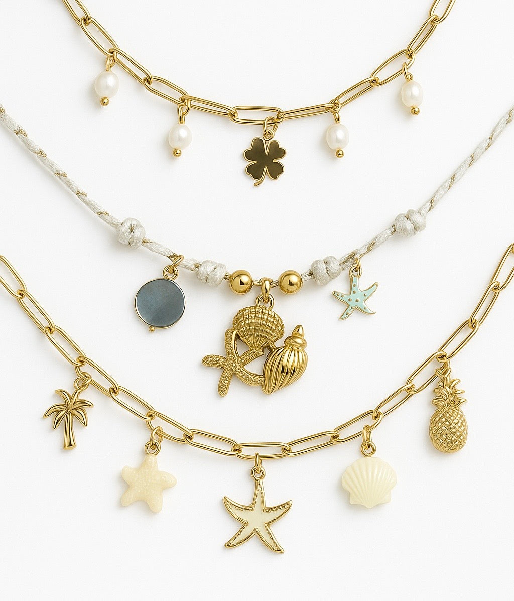 Collection de bracelets en acier inoxydable doré avec charms coquillage, étoile de mer, ananas, palmier et perles.
