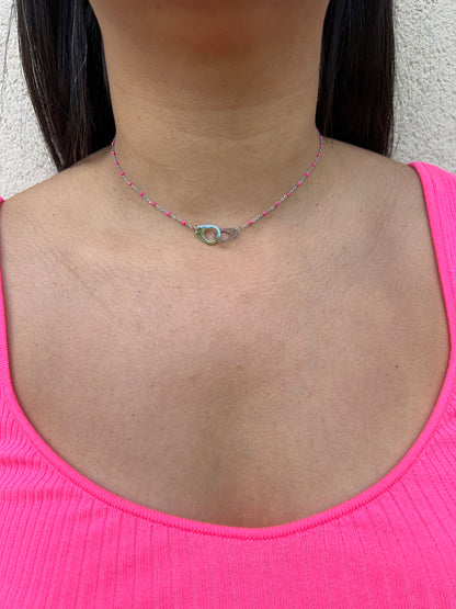 Collier en acier inoxydable argenté, orné de perles roses et d'un fermoir design, porté autour du cou féminin. Bijou moderne et élégant de la collection Bisou Bijoux Paris.