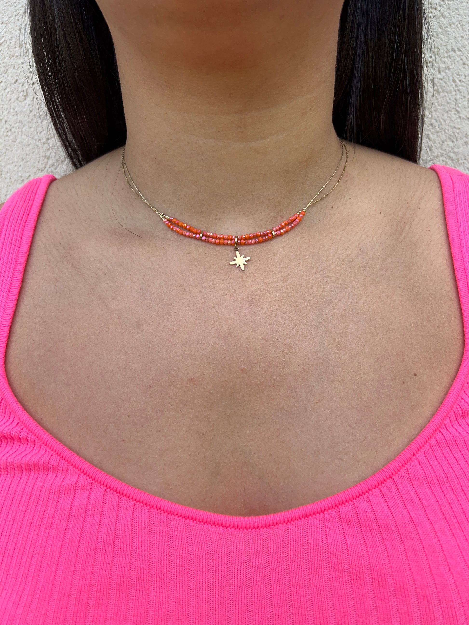 Collier double rang en acier inoxydable doré, orné de perles orange et d'un pendentif étoile délicat, porté autour du cou féminin. Bijou coloré et élégant de la collection Bisou Bijoux Paris.