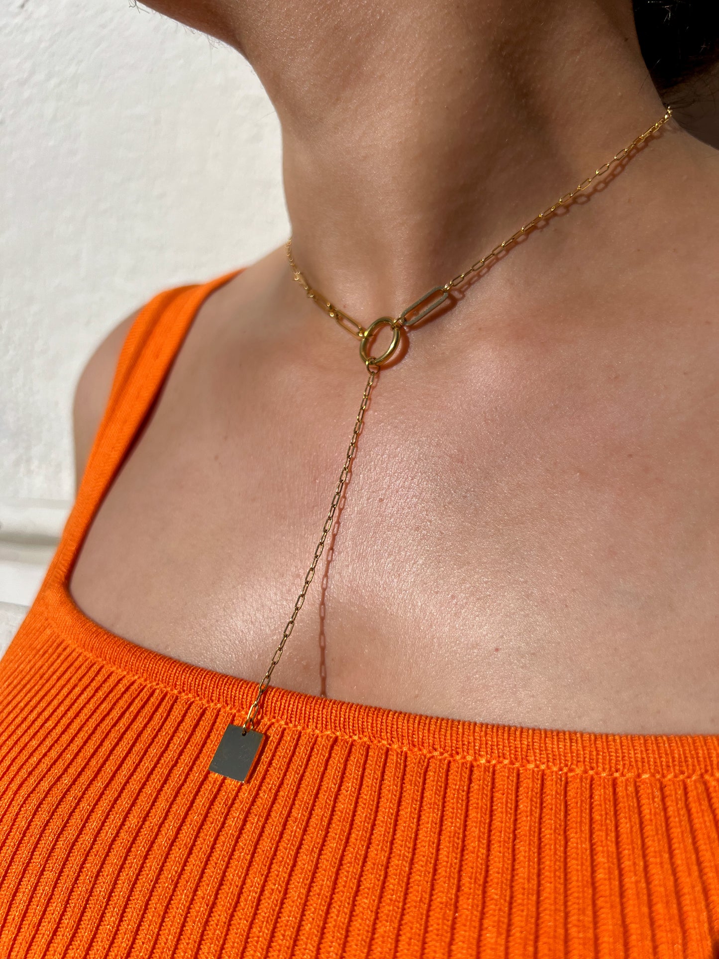 Collier ras de cou en acier inoxydable doré au design minimaliste avec un pendentif rectangulaire et une chaîne tombante, porté autour du cou féminin. Bijou moderne et élégant de la collection Bisou Bijoux Paris.