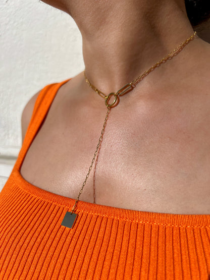 Collier ras de cou en acier inoxydable doré au design minimaliste avec un pendentif rectangulaire et une chaîne tombante, porté autour du cou féminin. Bijou moderne et élégant de la collection Bisou Bijoux Paris.