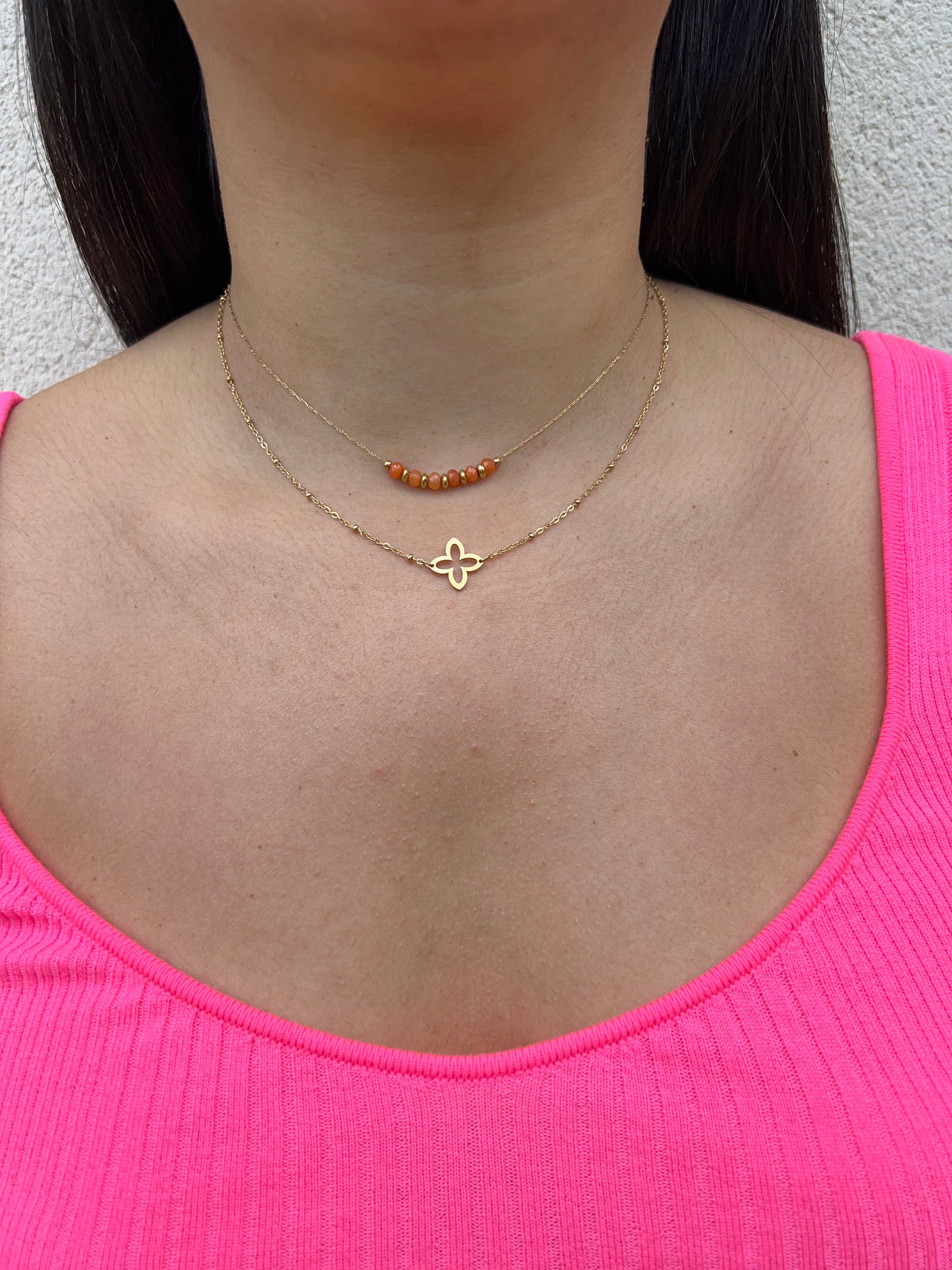 Collier double rang en acier inoxydable doré, composé d'un rang de perles orange et d'un pendentif fleur délicat, porté autour du cou féminin. Bijou raffiné et coloré de la collection Bisou Bijoux Paris.